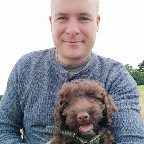Warren holding Humphrey as a curly chocolate cockapoo puppy, about twelve weeks old